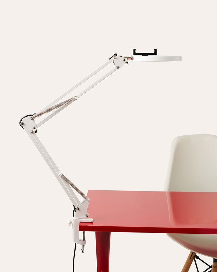 White adjustable Canvas LED desk lamp on a red table with a white chair in the background